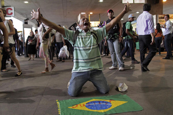 A man, with a Brazilian national flag laid out in front of him, shouts during a protest demanding improvements be made to the public transport system, at the bus station in the centre of Brasilia June 19, 2013. Brazilians fill streets with protest, violence